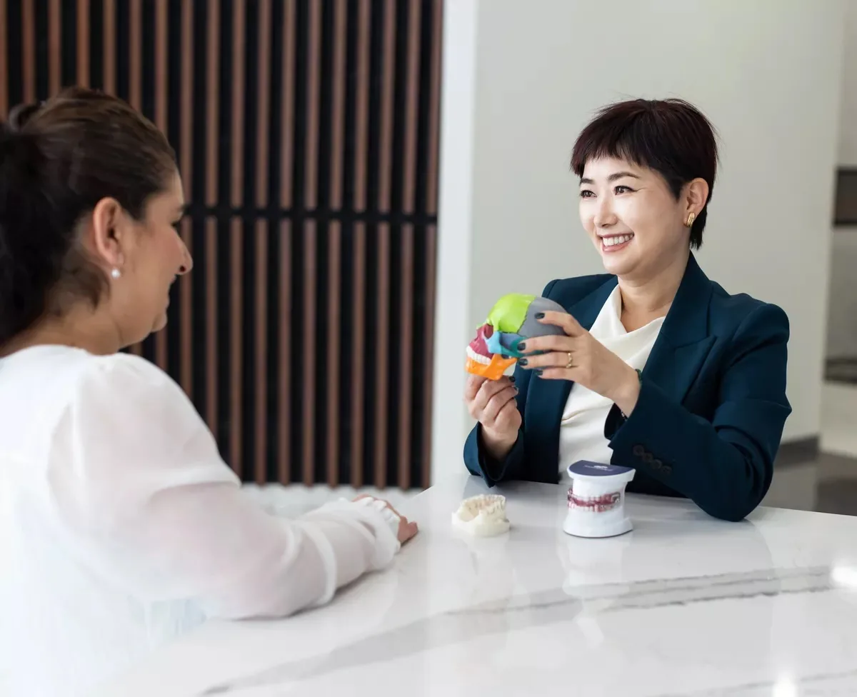 Dr. Hye Park reviewing a patient's bite and jaw with a dental model at Green Dentistry: Root and Restore in Alexandria, VA